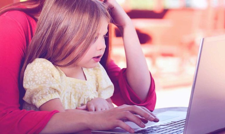 A young girl looking at a laptop screen with her mother.