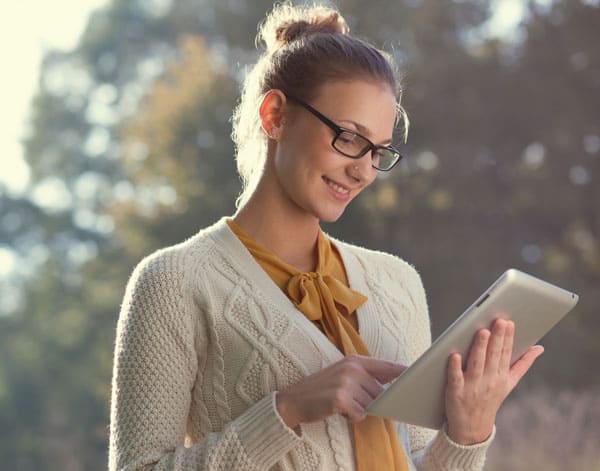 Desperately Seeking Genealogy Software: A Guide to Finding Your Perfect Match 4 A smiling woman with glasses, hair in a bun, gold blouse, and white cardigan sweater, looking at a tablet computer.