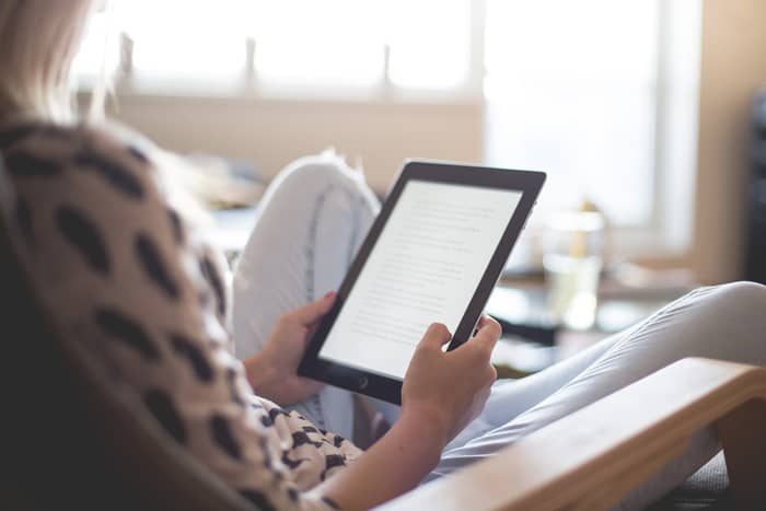 Where to Find Free Family History Books Online 4 A woman wearing jeans and a spotted blouse reading a book on an e-reader.