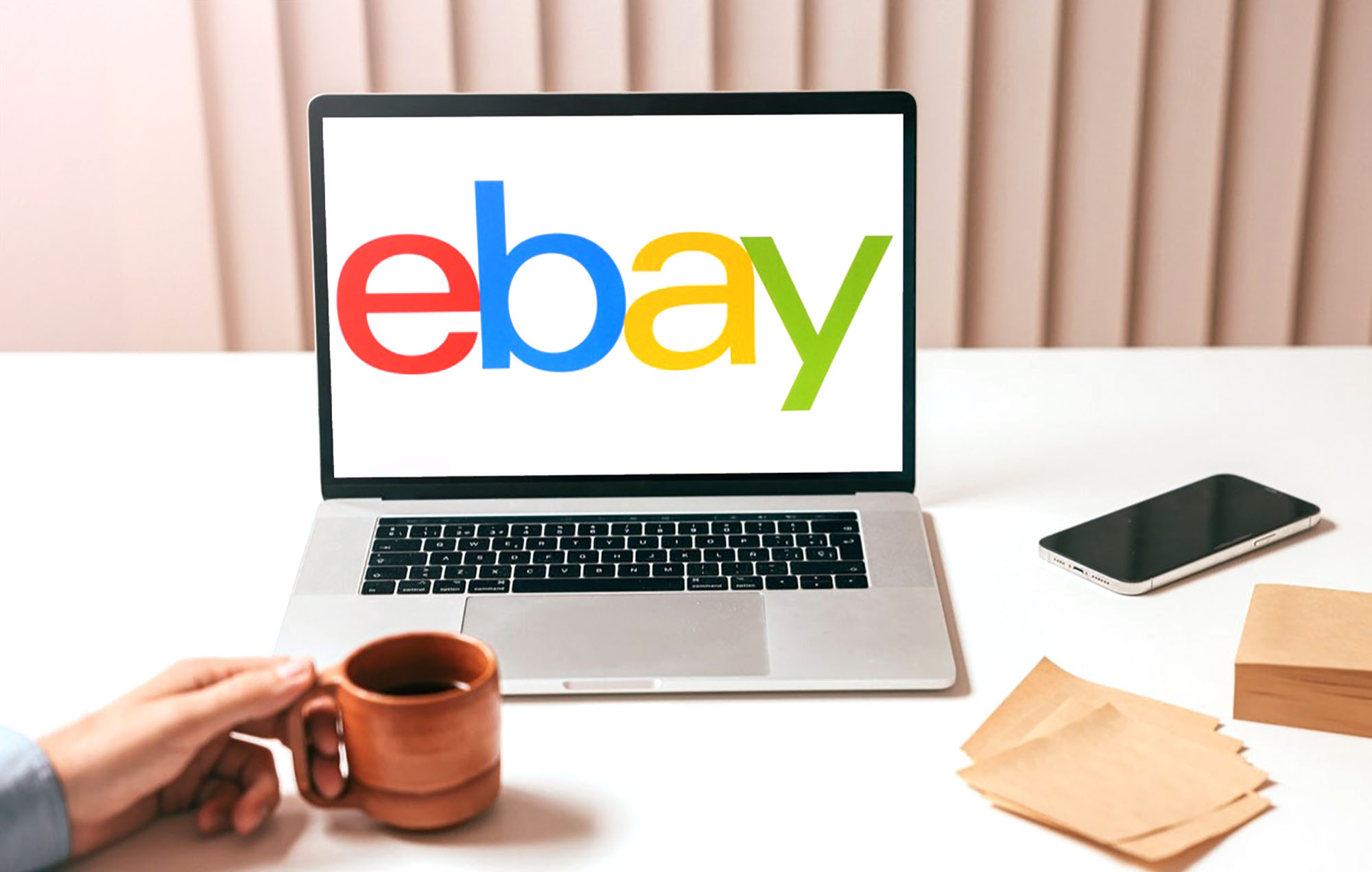 A hand holding a brown coffee cup in front of a laptop computer displaying the eBay logo.