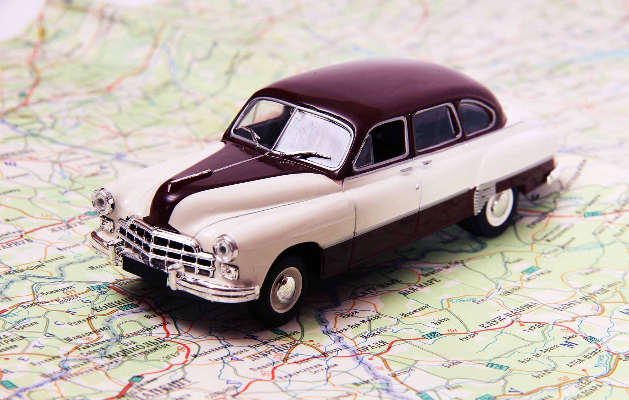 Maroon and beige retro toy car on a map signifying a road trip.