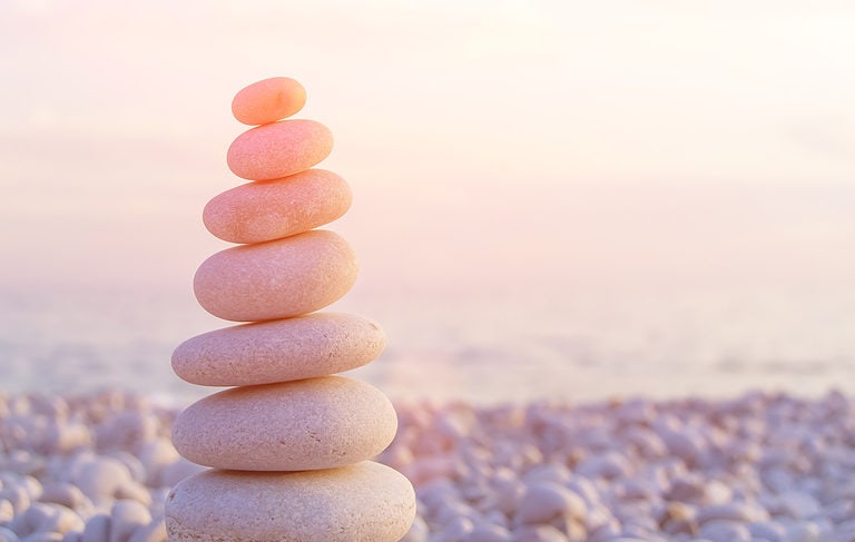 A stack of seven smooth flat stones on a rocky beach at sunset.